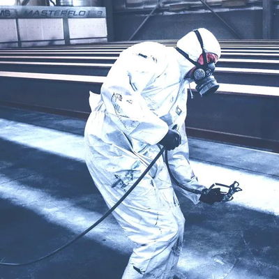 A man in a spray suit coating some machinery